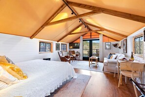 A cozy attic bedroom with a bed, seating area, and large windows. - Luxury Tented Cabin Glamping Escape, with River Access in Ingram, Texas (Hunt)