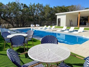 A pool area with lounge chairs and a table, surrounded by a fence and trees. - Luxury Tented Cabin Glamping Escape, with River Access in Ingram, Texas (Hunt)