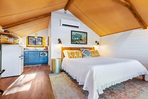 A bedroom with a bed, a wooden ceiling, a kitchen area, and a window. - Luxury Tented Cabin Glamping Escape, with River Access in Ingram, Texas (Hunt)