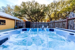 A hot tub with water jets, surrounded by a wooden fence and trees.