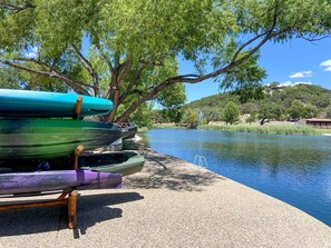 A calm lake with boats lined up on the shore, surrounded by trees and a hilly landscape. - Luxury Tented Cabin Glamping Escape, with River Access in Ingram, Texas (Hunt)