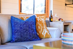A sofa with patterned cushions, a bottle, and a glass on a table. - Luxury Tented Cabin Glamping Escape, with River Access in Ingram, Texas (Hunt)