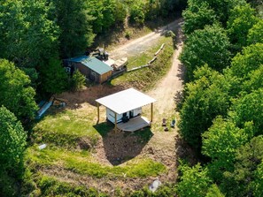 An aerial view of a cabin with a covered porch, surrounded by dense forest.