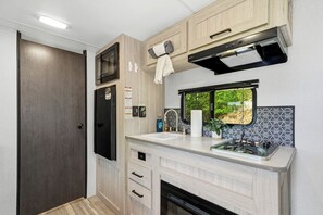 A compact RV kitchen with a microwave, stove, and a window with a view.