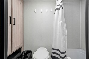 A small bathroom with a toilet, a shower curtain, and a trash bin.