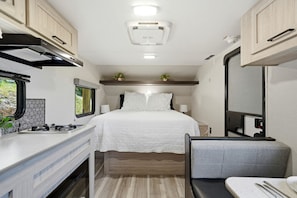 Interior compacto de RV com cozinha compacta, uma cama e uma pequena área de estar.