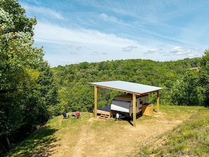 A campsite with a covered RV area, a picnic table, and a chair. - Charming Riverside Camper with Pool, Pickleball & Trails near Blue Ridge, Georgia (Blue Ridge)