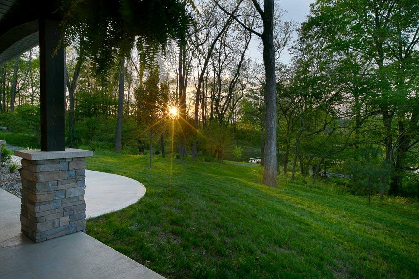 A well-maintained lawn with a stone pillar and a curved pathway leading to a covered area.