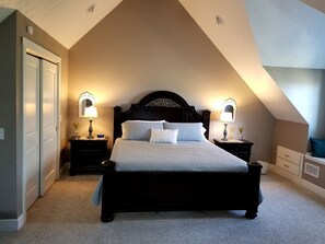 A bedroom with a dark wooden bed, two bedside tables with lamps, a door, and a sloped ceiling.