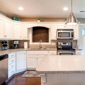 A kitchen with white cabinetry, a granite countertop, stainless steel appliances, and a pendant light.
