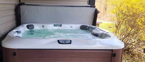 A hot tub with a control panel, surrounded by wooden walls and a garden with yellow flowers.