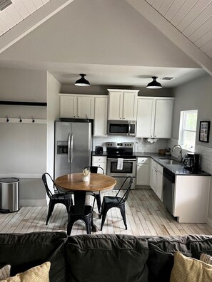 A compact kitchen with white cabinets, stainless steel appliances, a round wooden table, and black chairs. - Cozy Cabin in the Texan Countryside for Glamping Vacations in Wimberley (Wimberley)