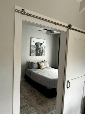 A bedroom with a bed, pillows, a rug, and a wall-mounted picture of a yak. - Cozy Cabin in the Texan Countryside for Glamping Vacations in Wimberley (Wimberley)