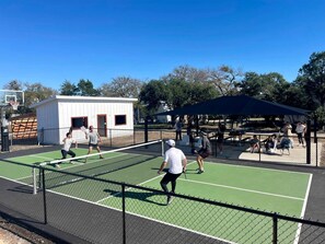 Una cancha de tenis al aire libre con red, un edificio pequeño y una zona de estar cubierta.