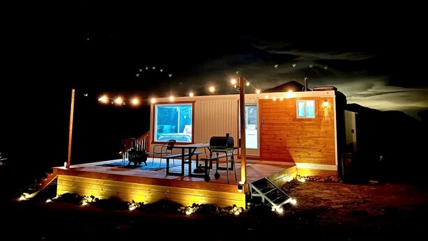 A wooden cabin with a deck, a table, chairs, and a window.