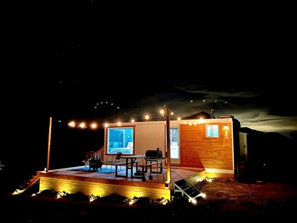 A wooden cabin with a deck, a table, chairs, and a window.