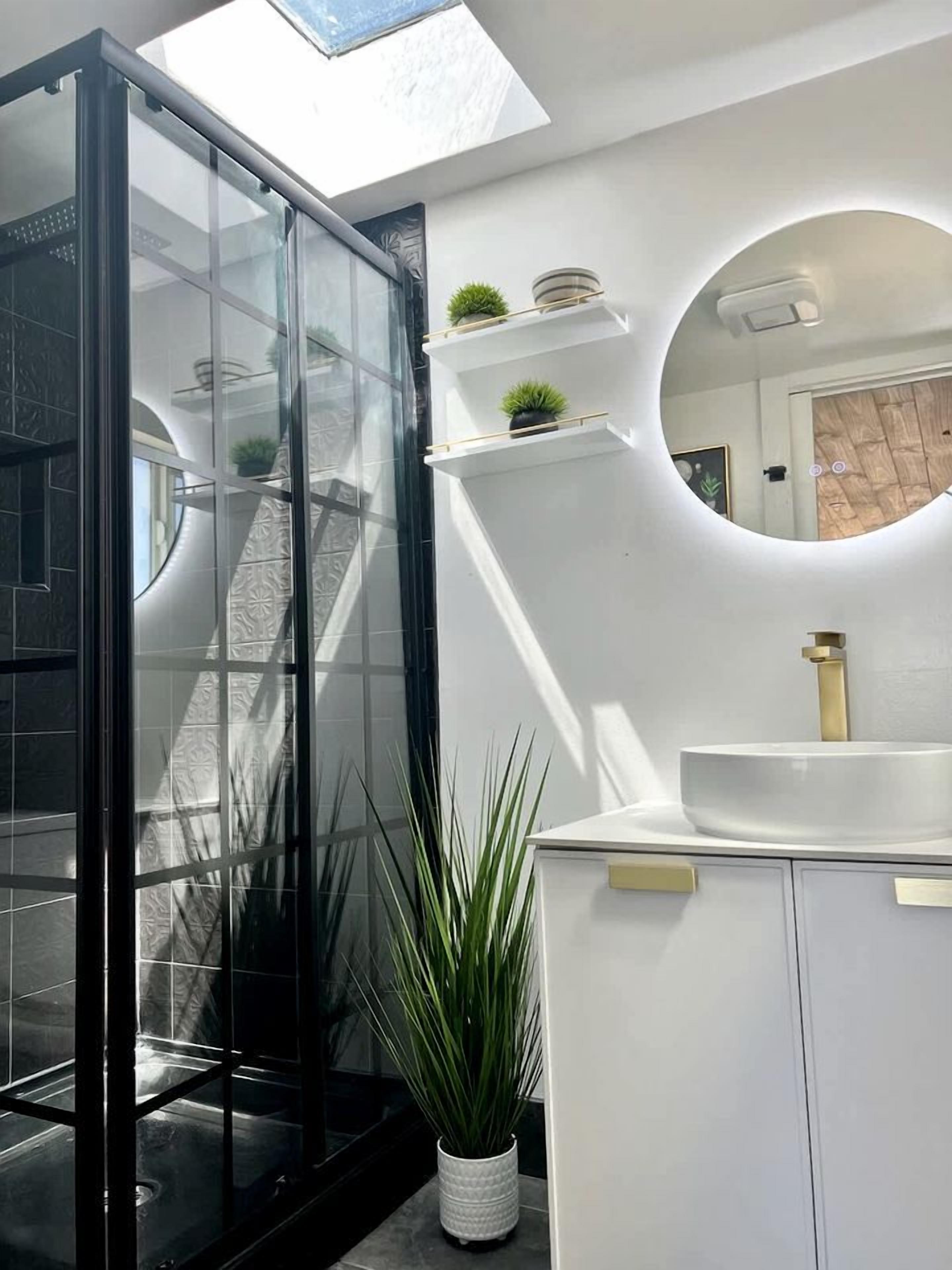 A modern bathroom with a glass shower enclosure, a white sink, and a skylight.