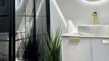 A modern bathroom with a glass shower enclosure, a white sink, and a skylight.