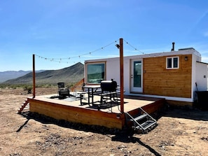 A small wooden cabin with a deck, a grill, and a chair. - Stunning Tiny House with Picnic Space, Barbecue and Fire Pit in Meadview, Arizona (Mohave Valley)