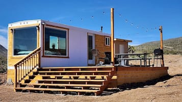 A small cabin with a wooden deck, a covered outdoor seating area, and a clear view of the surrounding landscape.