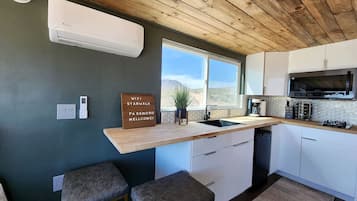 Een kleine keuken met een houten plafond, witte kastjes, een inbouwmagnetron en een barretje.
