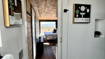 A hallway leading to a bedroom with a wooden ceiling, a bed, and two framed pictures on the walls.