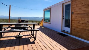A wooden deck with a table and chairs, a glass door, and a view of the mountains.