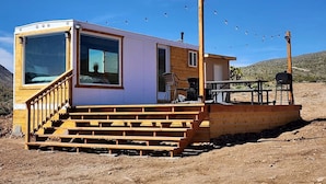A small cabin with a wooden deck, a covered outdoor seating area, and a clear view of the surrounding landscape.