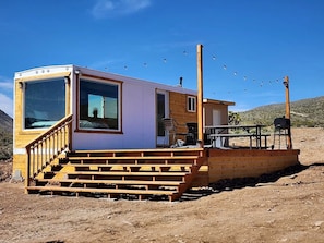 A small cabin with a wooden deck, a covered outdoor seating area, and a clear view of the surrounding landscape.