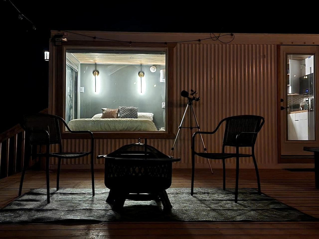 A cozy room with a bed, two chairs, a small table, and a tripod.