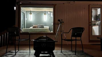 A cozy room with a bed, two chairs, a small table, and a tripod.