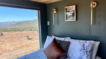 A bedroom with a large bed, a view of a desert landscape, and a framed picture on the wall.