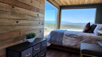 A bedroom with a wooden wall, a bed with a view, a nightstand, and a window.