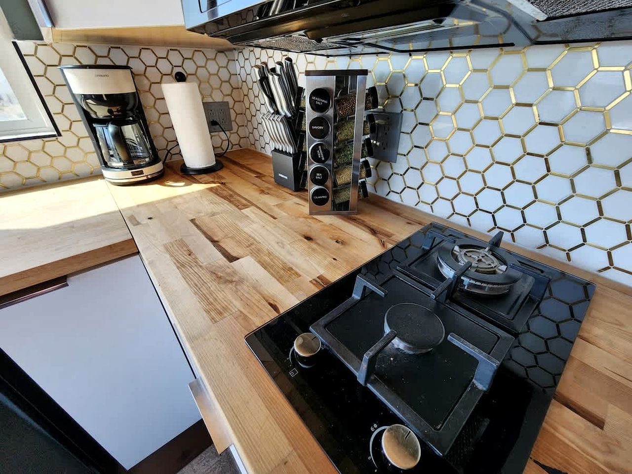 A compact kitchen with a built-in stove, a coffee maker, and a spice rack.