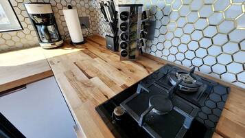A compact kitchen with a built-in stove, a coffee maker, and a spice rack.