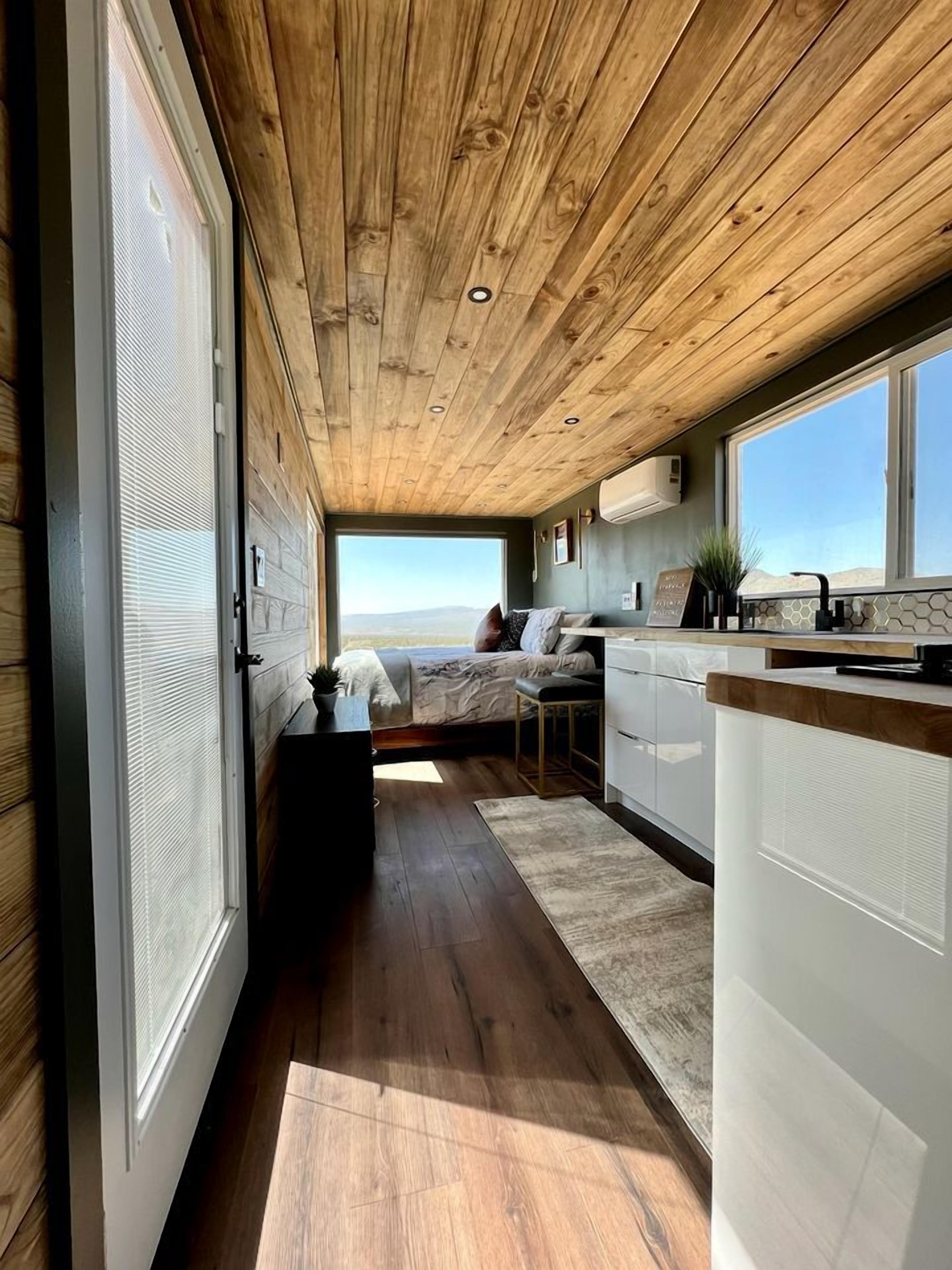 A modern interior with a wooden ceiling, a kitchen area, a seating area with a view, and a large window.
