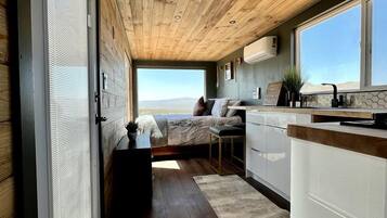 A modern interior with a wooden ceiling, a kitchen area, a seating area with a view, and a large window.