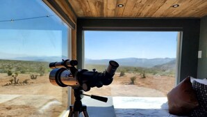 A telescope on a tripod in a room with a large window overlooking a desert landscape.