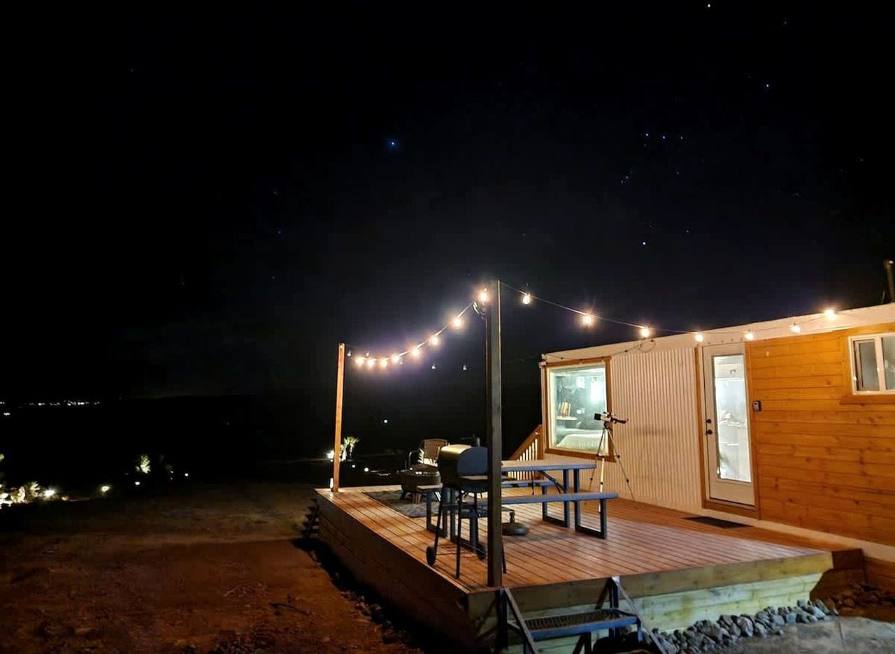 Eine Holzhütte mit einer Terrasse, Sitzgelegenheiten im Freien und einem Teleskop.