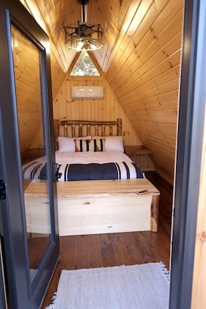 Quarto de madeira com cama, luminária no teto e porta de madeira.