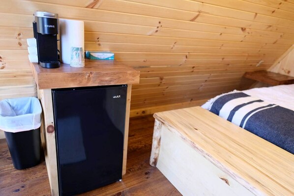 Una habitación compacta con un refrigerador negro pequeño, una cafetera y un cesto de basura.