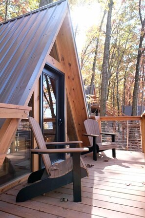 A wooden cabin with a sloped roof, a glass door, and two wooden chairs on a deck. - Secluded A-Frame Incredible for Water Activities by Tappan Lake in Ohio (Deersville)