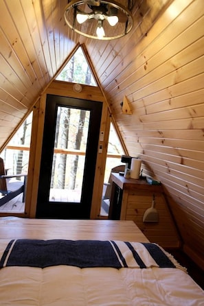 Um quarto de sótão aconchegante com uma cama, uma escrivaninha e uma janela com vista para árvores.