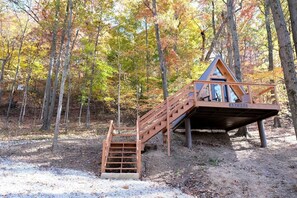 A wooden cabin with a staircase leading to a deck, surrounded by trees in autumn colors.