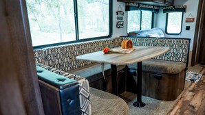 A cozy RV interior with a dining table, cushioned seating, and a window with a view of trees. - Texas Hill Country Glamping Caravan for a Nature Escape near Hamilton Creek (Marble Falls)