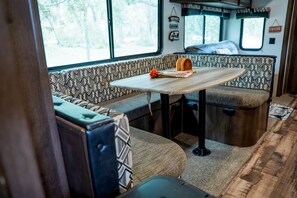 Ein gemütliches Wohnmobil-Interieur mit Esstisch, gepolsterten Sitzgelegenheiten und einem Fenster mit Blick auf Bäume.