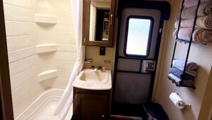 A compact bathroom with a toilet, sink, and a small window. - Texas Hill Country Glamping Caravan for a Nature Escape near Hamilton Creek (Marble Falls)