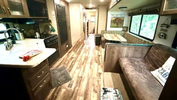 A compact RV interior with a kitchenette, a seating area, and a window.