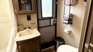 A compact RV bathroom with a sink, toilet, and a small window.