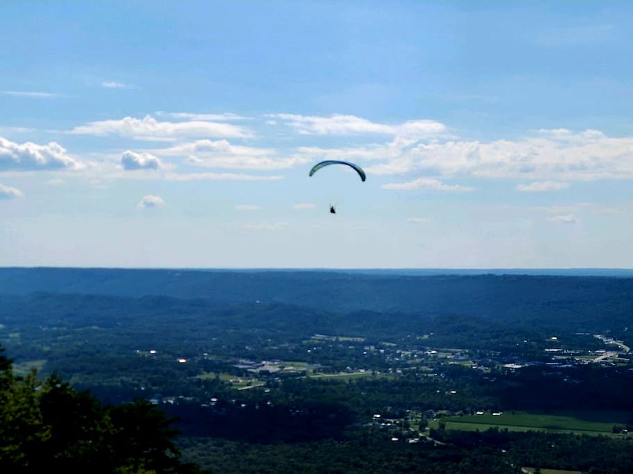 A person paragliding over a landscape with a clear sky.